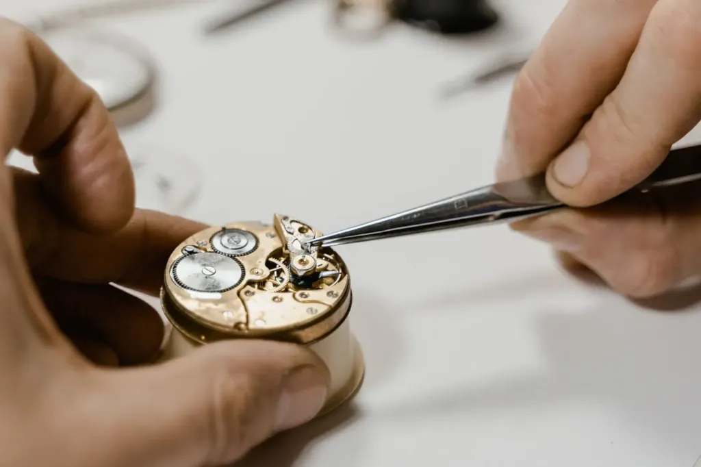 Handen met een pincet aan het uurwerk van een horloge tijdens een reparatie